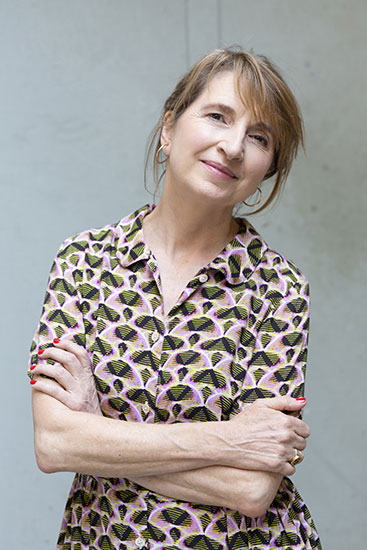Pascale Hugues blickt lächelnd in die Kamera, sie trägt ein leichtes Sommerkleid mit Muster. Sie wirkt entspannt und freundlich.